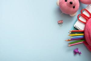 Teddy bear and colorful stationary with backpack on colored background. Copy space. Top view, flat lay photo