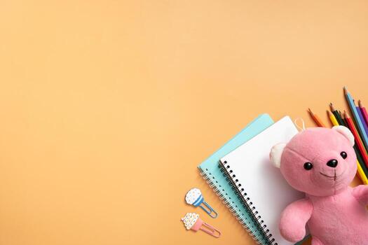 Notebooks, teddy bear and stationary on colored background. Copy space. Kids work space top view, flat lay. Online learning concept photo