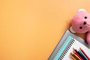 Stationary and laptop with teddy bear on colored background. Copy space. Kids work space top view, flat lay. Online learning concept photo