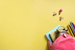 backpack with notepads and alarm clock with teddy bear and colorful pensils on colored background with copy space. Back to school concept photo