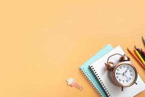 Notebooks, alarm clock and stationary on colored background. Copy space. Kids work space top view, flat lay. Online learning concept photo