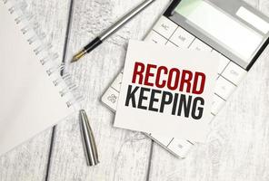 Text RECORD KEEPING on paper card and calculator on wooden background photo