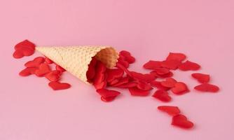 Creative photo of empty waffle cones with scattered red hearts on a pink background. The concept of love, summer, spring