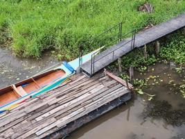 Long tail boat is floating near the wooden pontoon. photo