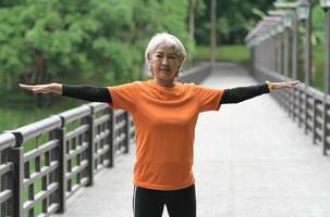 una mujer asiática jubilada con una camiseta naranja hace ejercicio al aire libre, corre, levanta pesas, se estira. foto