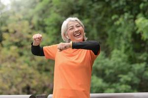 A retired Asian woman wearing an orange T-shirt is exercising outdoors, running, lifting dumbbells, stretching. photo
