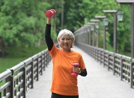 A retired Asian woman wearing an orange T-shirt is exercising outdoors, running, lifting dumbbells, stretching. photo