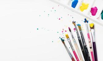 Art Paint brushes and palette with colorful paint splatter on white canvas paper. Copy space photo