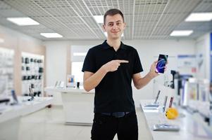 vendedor hombre consultor profesional de telefonía móvil en tienda de tecnología o tienda sostenga un nuevo teléfono inteligente a mano y muestre el dedo a la pantalla. foto