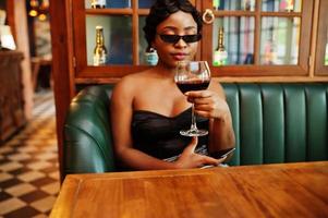 Portrait of african american woman, retro hairstyle posing at restaurant with glass of wine. photo