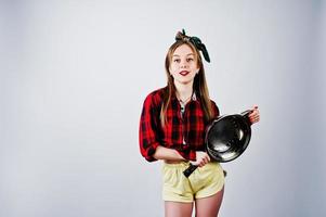 Young funny housewife in checkered shirt and yellow shorts pin up style with frying pan isolated on white background. photo