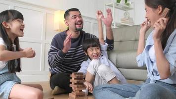 Fröhliche asiatische schöne thailändische Familienaktivität, Eltern, Vater, Mutter und Kinder haben Spaß beim Spielen und fröhliche Holzspielzeugblöcke zusammen auf dem Wohnzimmerboden, Freizeitwochenende und häuslichem Wohlbefinden. video