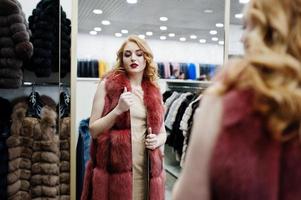 Elegance blonde girl in fur coat at the store of fur coats and leather jackets. photo