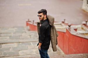 Indian stylish man at black shirt and jacket with sunglasses posed outdoor. photo