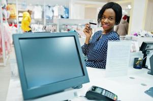 feliz cliente afroamericana con bolsas de compras de colores pagando con tarjeta de crédito cerca de la terminal de efectivo con pos. foto