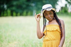 Portrait of gorgeous african american woman 20s in wear in yellow dress and summer hat posing at green grass in park. photo