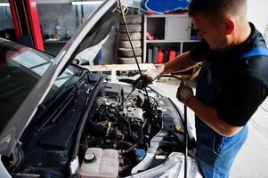 Car repair and maintenance theme. Mechanic in uniform working in auto service, checking engine. photo