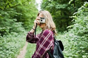 Portrait of a gorgeous young girl in tartan shirt taking pictures with camera in the forest. photo