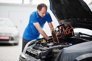 Car repair and maintenance theme. Mechanic in uniform working in auto service, checking engine. photo