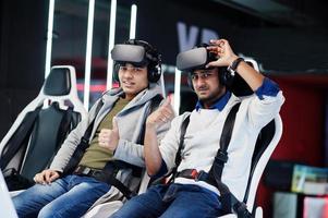 Two young indian people having fun with a new technology of a vr headset at virtual reality simulator. They happy and show thumb up. photo