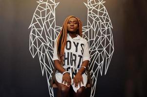 Beautiful african woman in stylish casual clothes posing against angel wings wall. photo