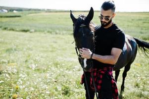 Arab tall beard man wear in black and sunglasses with arabian horse. photo