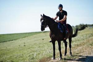 El hombre árabe de barba alta usa casco negro, monta un caballo árabe. foto