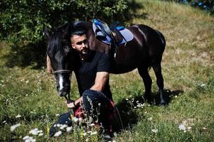 Hombre árabe de barba alta vestido de negro con caballo árabe. foto