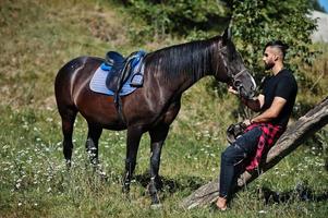 Hombre árabe de barba alta vestido de negro con caballo árabe. foto