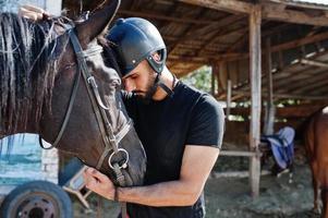 Arab tall beard man wear in black helmet with arabian horse. photo