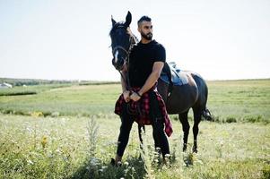 Hombre árabe de barba alta vestido de negro con caballo árabe. foto