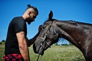 Hombre árabe de barba alta vestido de negro con caballo árabe. foto