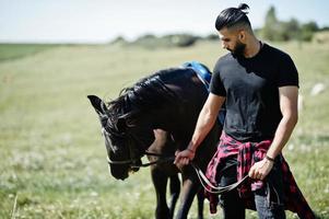 Arab tall beard man wear in black with arabian horse.