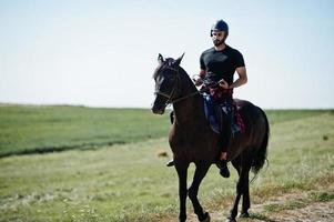 Arab tall beard man wear in black helmet, ride arabian horse. photo