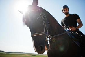 El hombre árabe de barba alta usa casco negro, monta un caballo árabe. foto