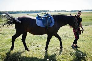 Hombre árabe de barba alta vestido de negro con caballo árabe. foto