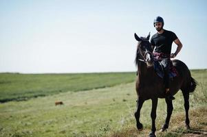 El hombre árabe de barba alta usa casco negro, monta un caballo árabe. foto