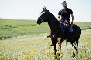 El hombre árabe de barba alta usa un caballo árabe negro. foto