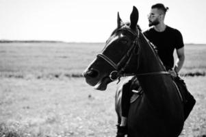 Arab tall beard man wear in black and sunglasses ride arabian horse. photo