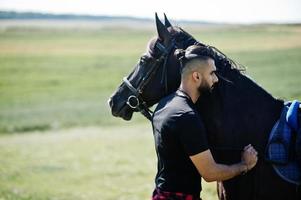 Arab tall beard man wear in black with arabian horse. photo