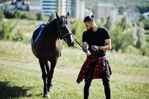 Hombre árabe de barba alta vestido de negro con caballo árabe. foto