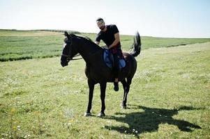 Arab tall beard man wear in black and sunglasses ride arabian horse. photo