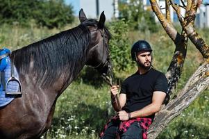 Arab tall beard man wear in black helmet with arabian horse. photo