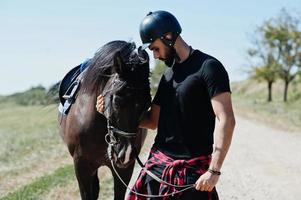 Arab tall beard man wear in black helmet with arabian horse. photo