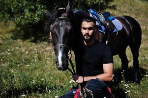 Hombre árabe de barba alta vestido de negro con caballo árabe. foto