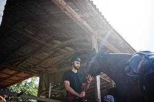 Arab tall beard man wear in black helmet with arabian horse. photo