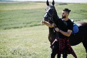 Hombre árabe de barba alta vestido de negro con caballo árabe. foto