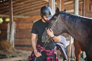 Arab tall beard man wear in black helmet with arabian horse. photo