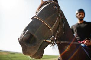 El hombre árabe de barba alta usa casco negro, monta un caballo árabe. foto