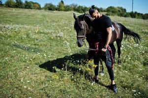 Hombre árabe de barba alta vestido de negro con caballo árabe. foto